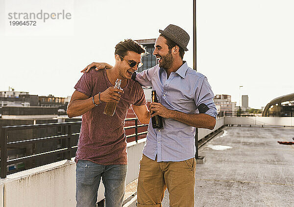 Lächelnde Männer  die Bier trinken und auf dem Dach genießen
