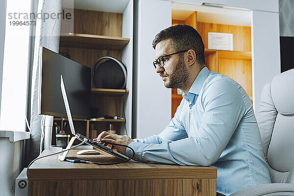 Freelancer wearing eyeglasses and working on laptop at home office