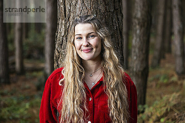 Lächelnde junge schöne Frau in der Nähe eines Baumes im Wald