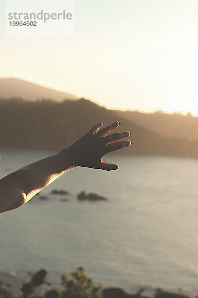 Hand eines jungen Mannes  der bei Sonnenuntergang das Meer erreicht