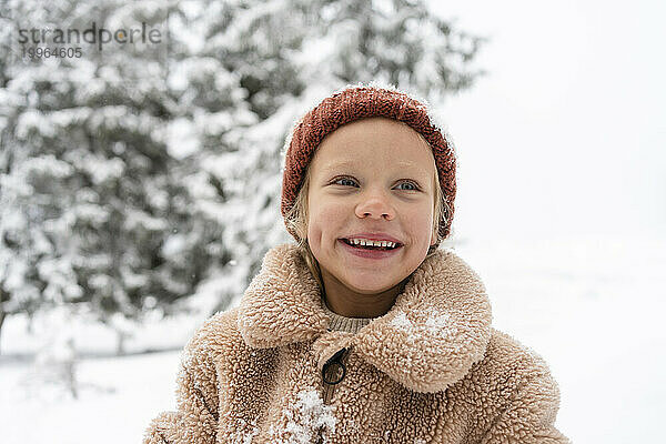 Happy girl wearing knit hat in winter forest