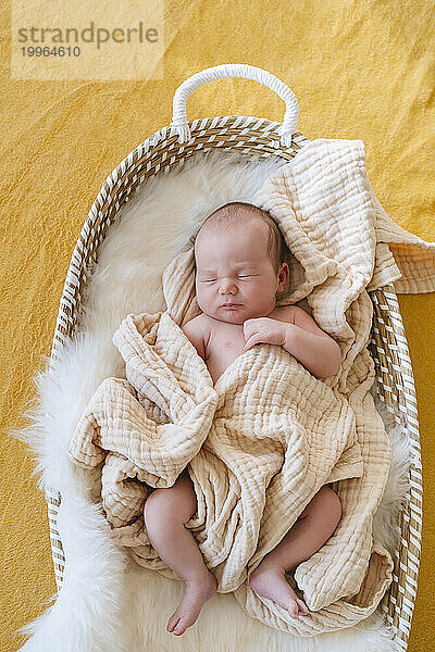 Cute baby boy sleeping in basket at home