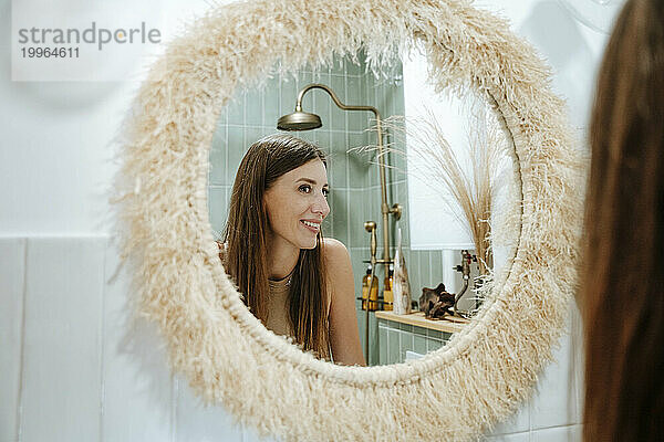 Lächelnde Frau  die sich im Badezimmerspiegel betrachtet