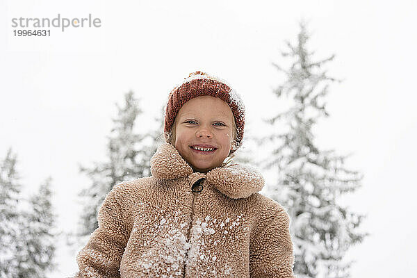 Lächelndes Mädchen mit Strickmütze und stehend im Winterwald