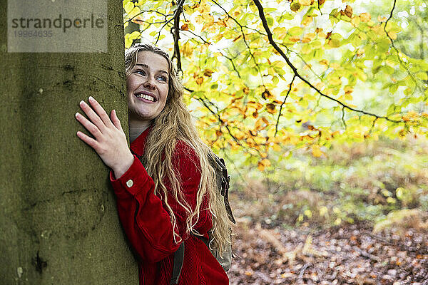 Lächelnde schöne Frau umarmt Baum im Wald von Cannock Chase