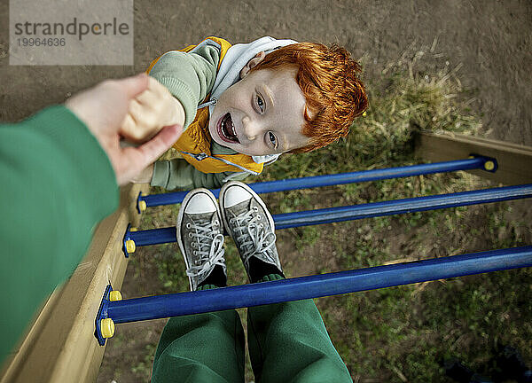 Verspielter Junge hält Mutters Hand auf Leiter auf Spielplatz