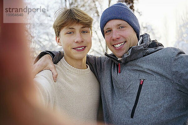 Lächelnder Teenager  der im Winter ein Selfie mit seinem Vater macht