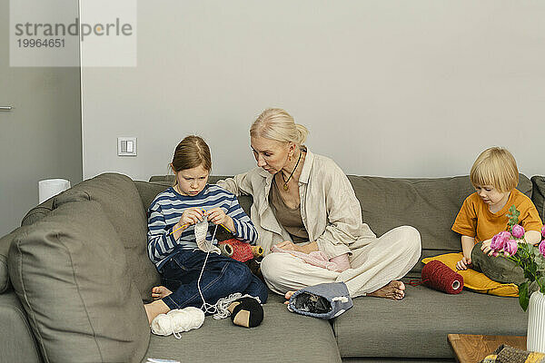 Großmutter sitzt mit Enkelkindern und strickt zu Hause auf dem Sofa