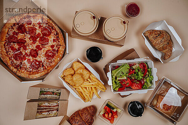 Fastfood und Salat mit Pizza vor beigem Hintergrund