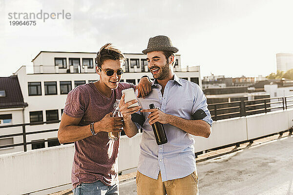 Glücklicher Mann zeigt einem Freund sein Smartphone auf dem Dach
