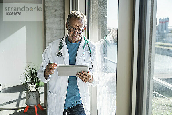 Leitender Arzt benutzt Tablet-PC am Fenster