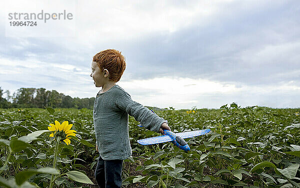 Rothaariger Junge spielt mit Spielzeugflugzeug im Feld