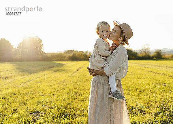 Schwangere Mutter küsst Tochter im Feld bei Sonnenuntergang