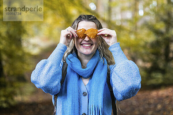 Happy woman covering eyes with leaves in forest