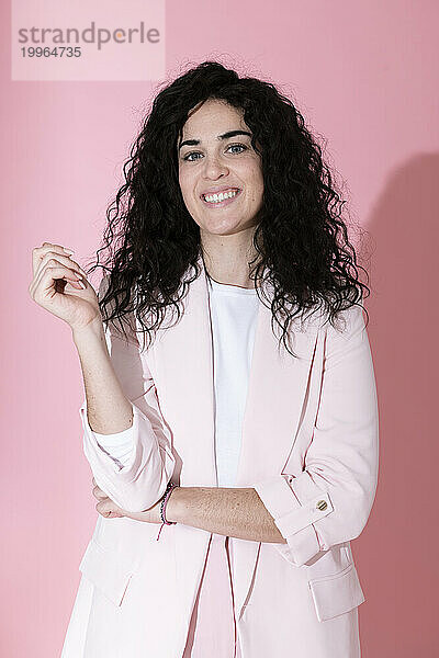 Smiling young woman wearing blazer and standing against pink background