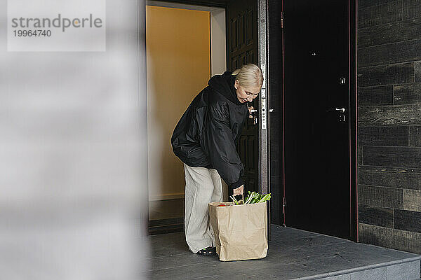 Lächelnde Frau holt eine Tüte Gemüse von der Veranda des Hauses