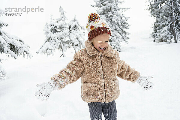 Glückliches Mädchen  das im Winterwald mit Schnee spielt