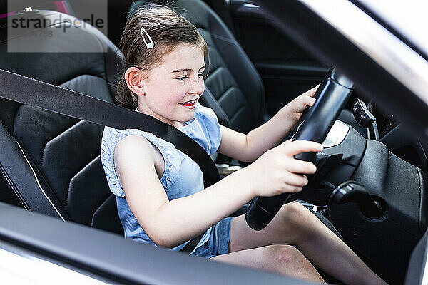 Aufgeregtes Mädchen mit Lenkrad im Auto sitzend