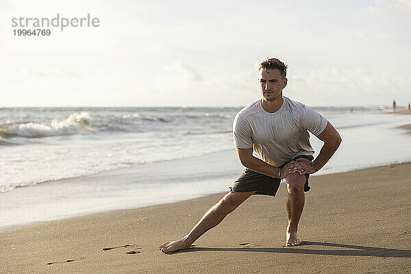 Young man doing stretching exercise at beach