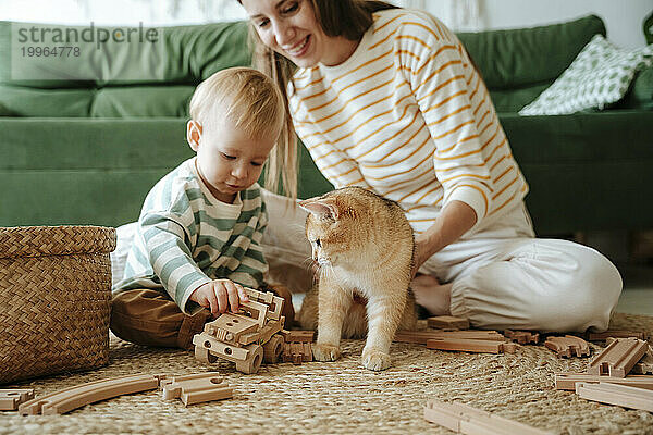 Mutter und Sohn mit Katze spielen zu Hause im Wohnzimmer