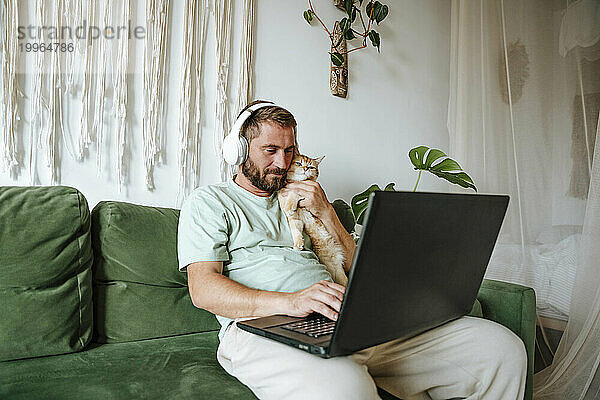 Man with cat sitting on the couch at home and using laptop