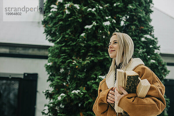 Lächelnde Frau trägt Winterjacke und trägt Brennholz