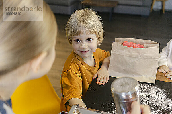 Lächelnder blonder Junge sitzt mit Schwestern am Esstisch