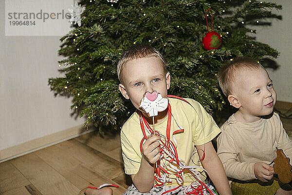 Junge hält Weihnachtsplätzchen in der Hand und sitzt mit seinem Bruder zu Hause