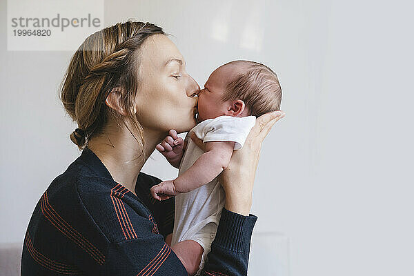 Mother kissing baby boy in front of wall