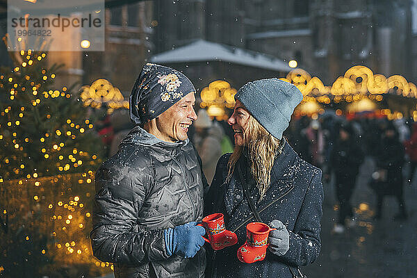 Glückliches Paar hält Tassen Punsch auf dem Weihnachtsmarkt