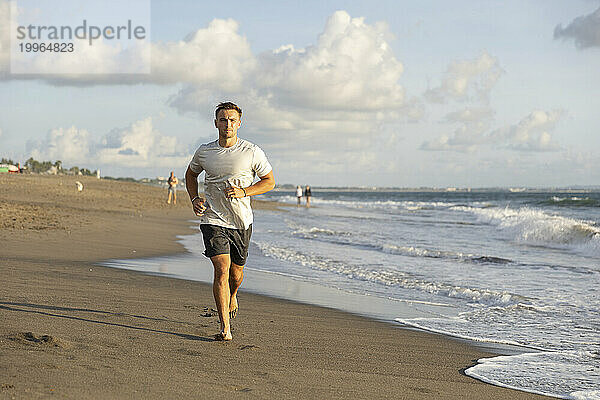 Junger Mann joggt am Strand am Meer