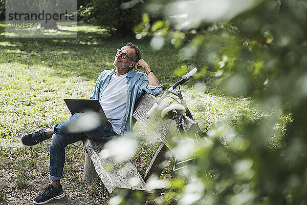 Nachdenklicher Mann mit Laptop sitzt auf Bank im Park