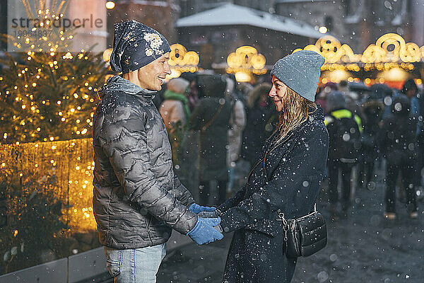 Glückliches Paar hält Händchen und steht im Winter auf dem Weihnachtsmarkt