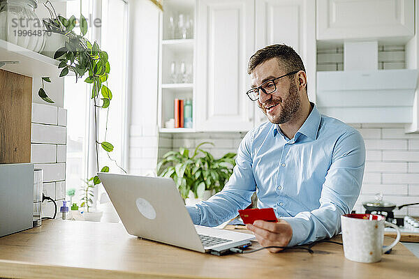 Glücklicher Freiberufler  der zu Hause online per Kreditkarte auf dem Laptop bezahlt