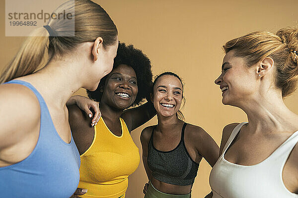 Happy multiracial female friends laughing against beige background