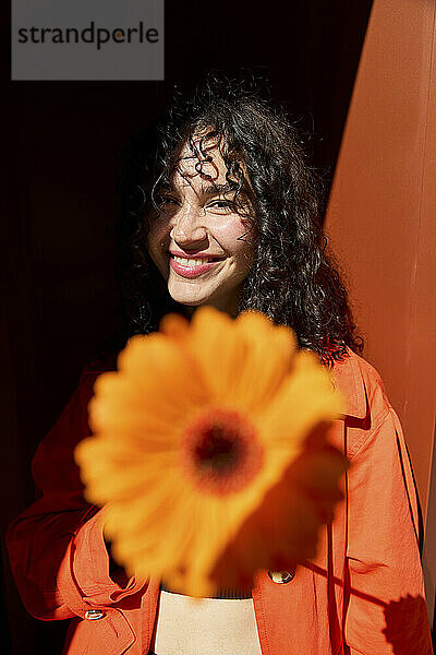 Lächelnde Frau mit Gerbera-Blume vor der Wand