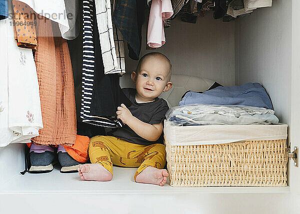 Netter Junge  der zu Hause mit Kleidung im Schrank spielt