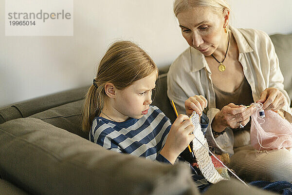 Konzentriertes Mädchen lernt zu Hause mit Großmutter das Stricken