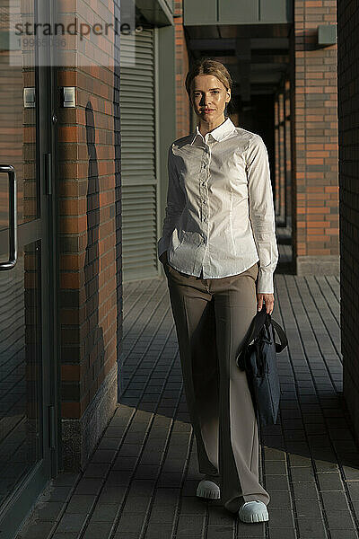 Selbstbewusste Geschäftsfrau mit Tasche steht auf Fußweg