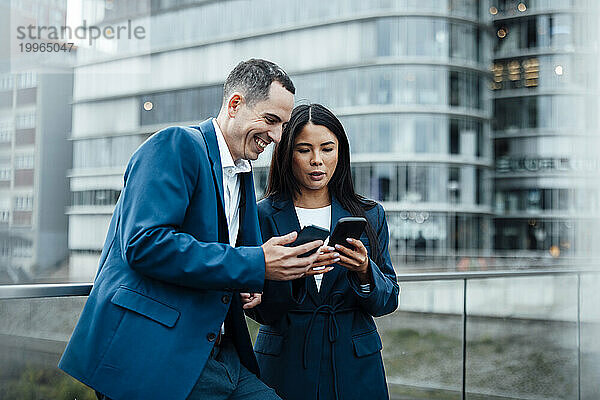 Glücklicher Geschäftsmann und Geschäftsfrau  die ihr Smartphone vor Gebäuden nutzen