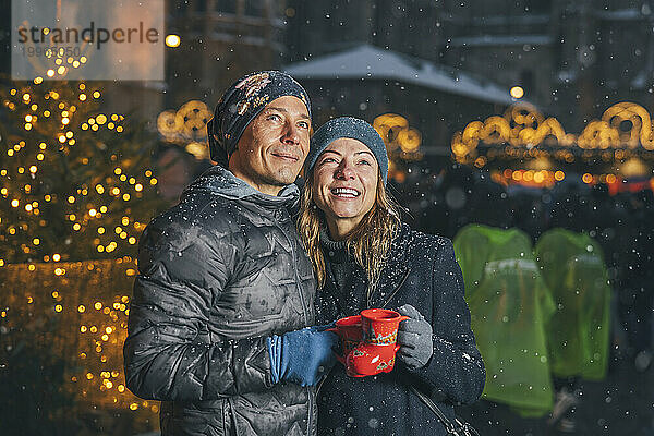 Lächelnde Männer und Frauen halten Tassen mit Punschgetränk auf dem Weihnachtsmarkt