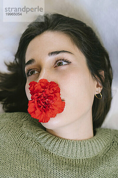 Contemplative woman with red flower over mouth against white background