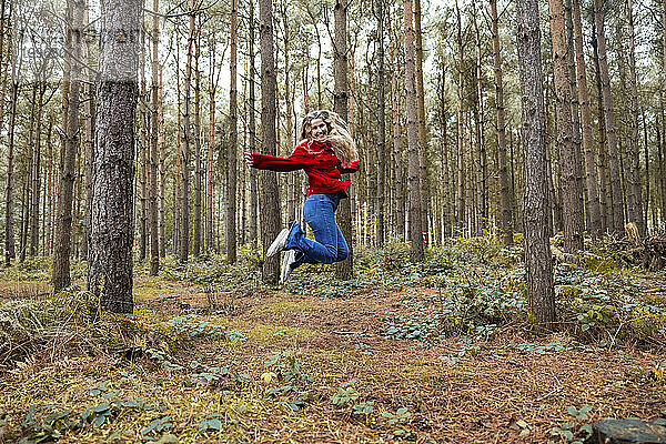 Fröhliche Frau springt in der Nähe von Bäumen im Wald von Cannock Chase