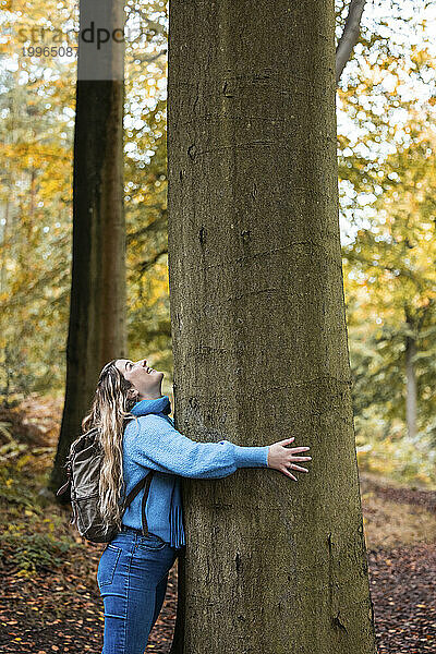 Glückliche junge Frau umarmt Baum im Wald von Cannock Chase