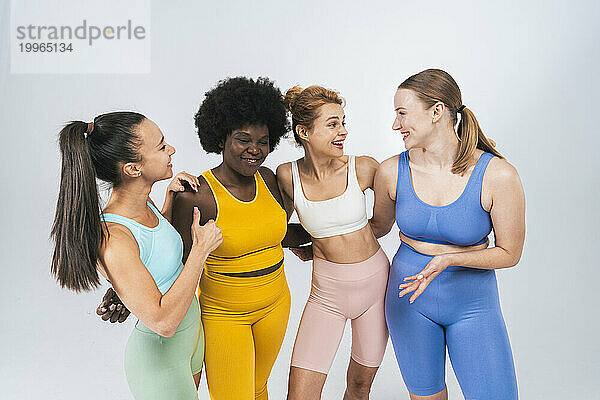 Happy multiracial female friends talking against white background