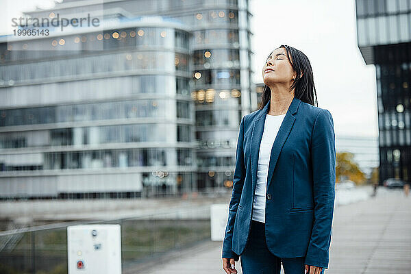 Businesswoman standing with eyes closed near buildings