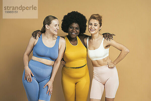 Smiling woman with arms around female friends against beige background