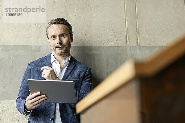 Selbstbewusster Geschäftsmann mit Tablet-PC vor der Wand