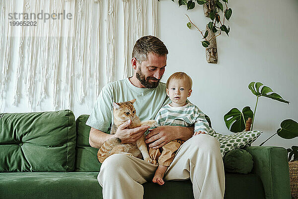 Vater und Sohn sitzen mit Katze auf der Couch im Wohnzimmer zu Hause