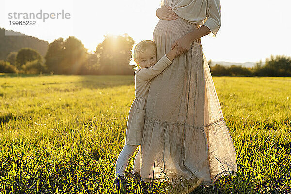 Loving pregnant mother holding daughter's hand in field